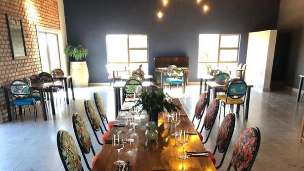 A dining area with a long wooden table set for a meal, surrounded by chairs with colorful floral upholstery. - Klein Karoo Game Lodge (De Hoop)