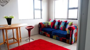 A cozy room with a wooden table, a red chair, a colorful sofa, and a red rug. - Klein Karoo Game Lodge (De Hoop)