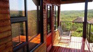 A wooden cabin with large windows, a deck, and outdoor furniture. - Klein Karoo Game Lodge (De Hoop)