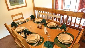 A dining table set for six with green placemats, white plates, and silverware.