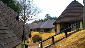 A rural setting with traditional thatched-roof houses and a modern building with a staircase leading up a hill.