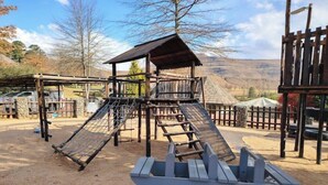 A playground with a wooden climbing structure, a slide, and a boat-shaped play area.