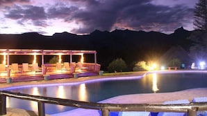 A pool area with a covered seating area and a view of mountains in the background.