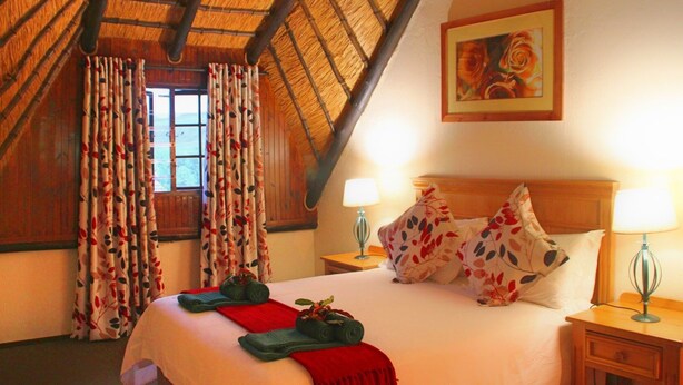 A hotel room with a bed, floral curtains, a painting, and two bedside lamps.