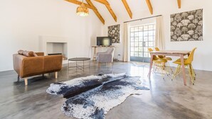 Ein geräumiges Wohnzimmer mit hohen Decken, einem Kamin, einem Fernseher und einem Essbereich mit gelben Stühlen.