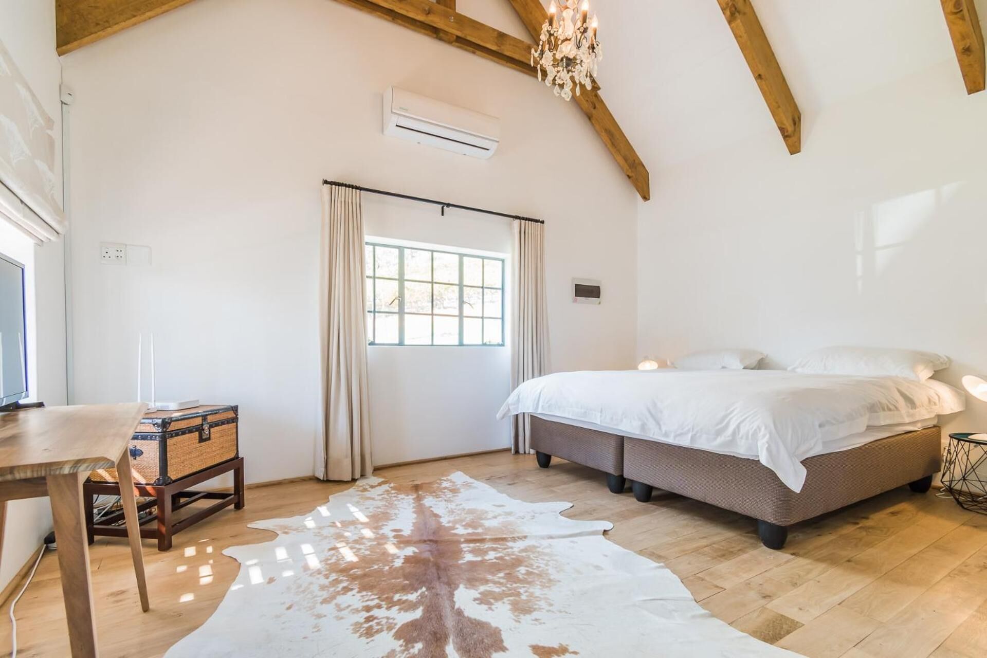 A bedroom with a large bed, a desk, a cowhide rug, and a chandelier.