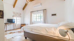 Ein Schlafzimmer mit einem großen Bett, einem Schreibtisch, einem Fernseher und einem Fenster mit Vorhängen.
