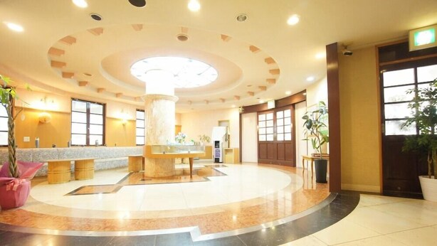 A spacious lobby with a central marble column, large windows, and potted plants. - Hotel San Marco (Daito)