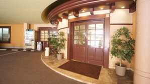 A hotel entrance with a curved facade, a reception desk, and potted plants. - Hotel San Marco (Daito)