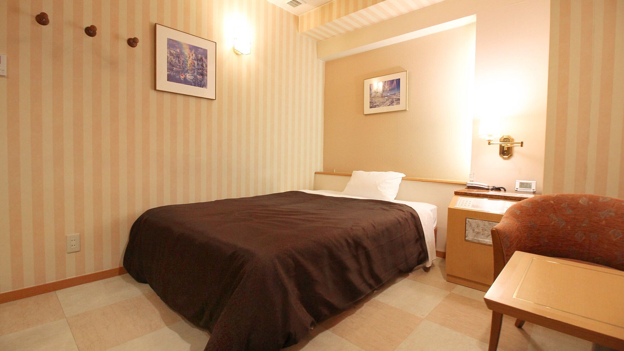 Habitació d'hotel amb un llit, una petita taula de nit, una cadira i dos quadres penjats a la paret.
