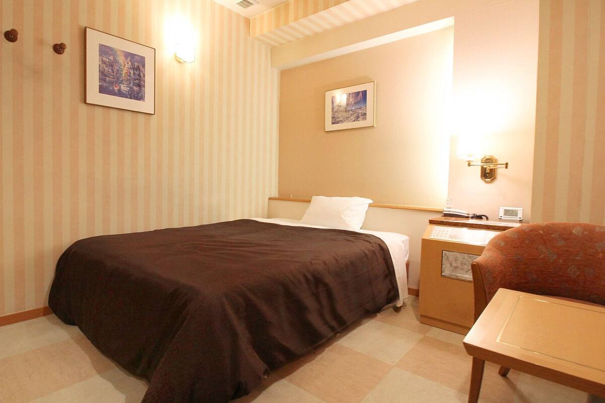 Une chambre d’hôtel avec un lit, une table de chevet, une chaise et deux tableaux encadrés au mur.