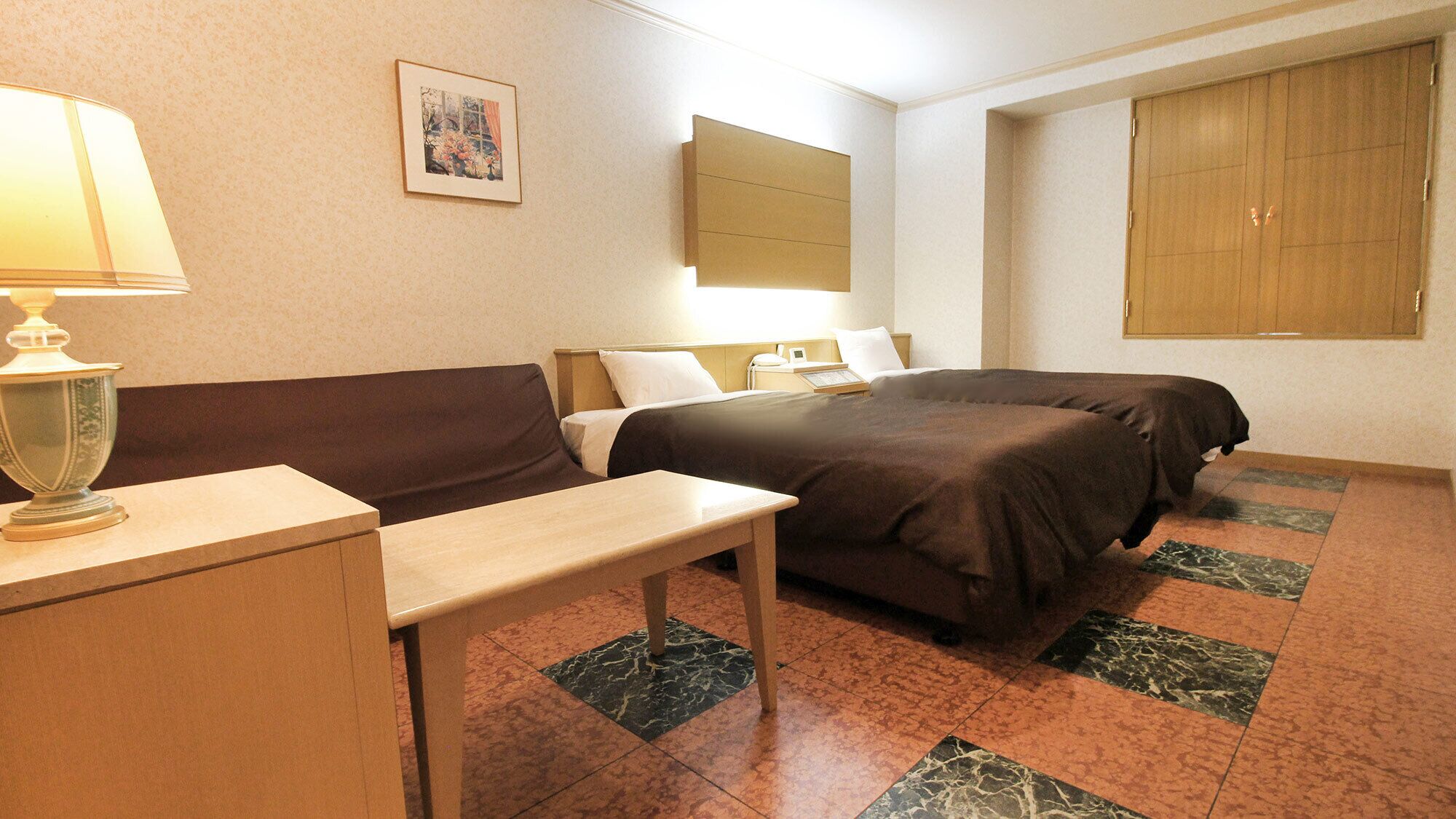 Habitació d'hotel amb llit, sofà, escriptori, làmpada, quadre a la paret i finestra.