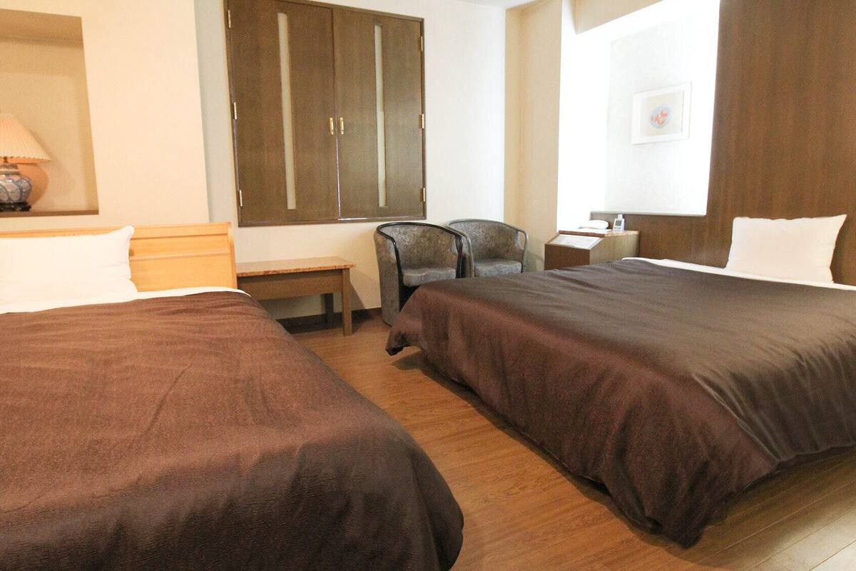 Une chambre d’hôtel avec deux lits, un bureau, une chaise, une armoire et une fenêtre.
