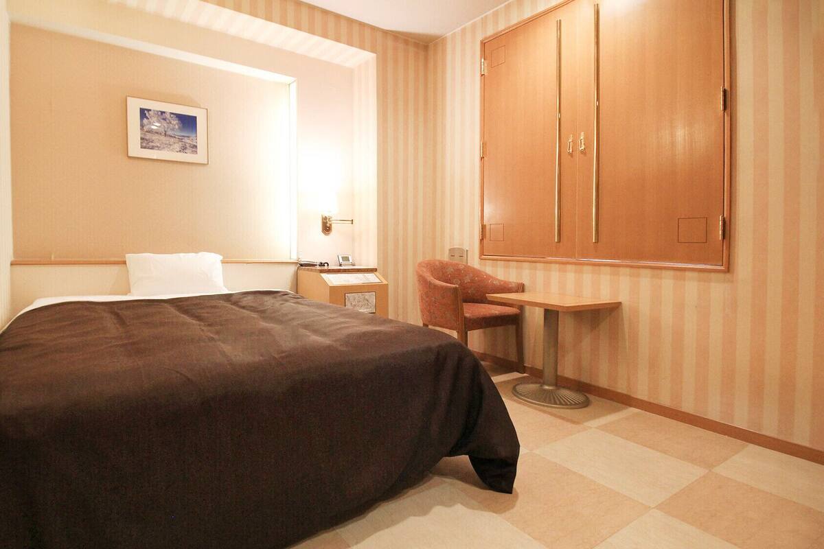 Une chambre d’hôtel comprenant un lit, un bureau, une chaise, une petite table, une armoire et un tableau encadré au mur.
