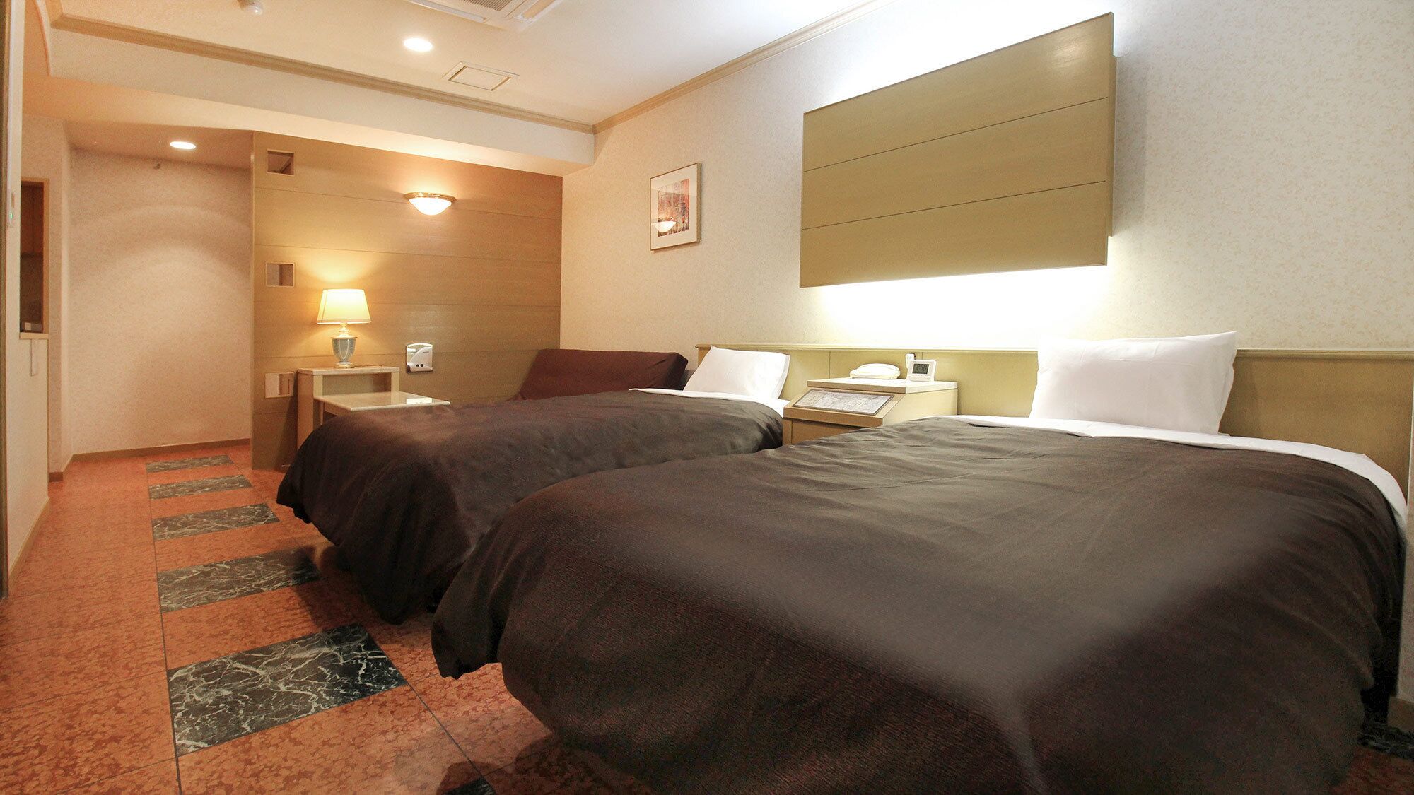 Habitació d'hotel amb dos llits, una taula de nit, una làmpada, un quadre al mur i un sòl amb moqueta.