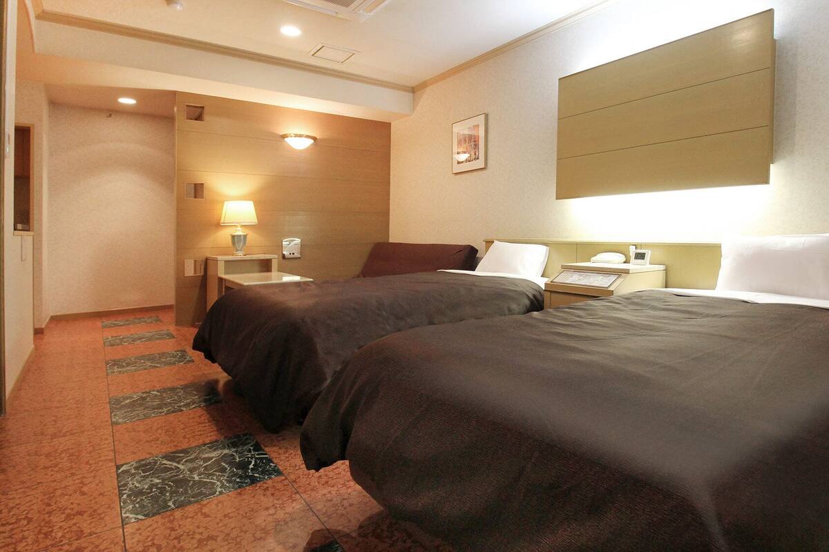 Une chambre d’hôtel avec deux lits, une table de chevet, une lampe, un tableau encadré au mur et un sol recouvert de moquette.