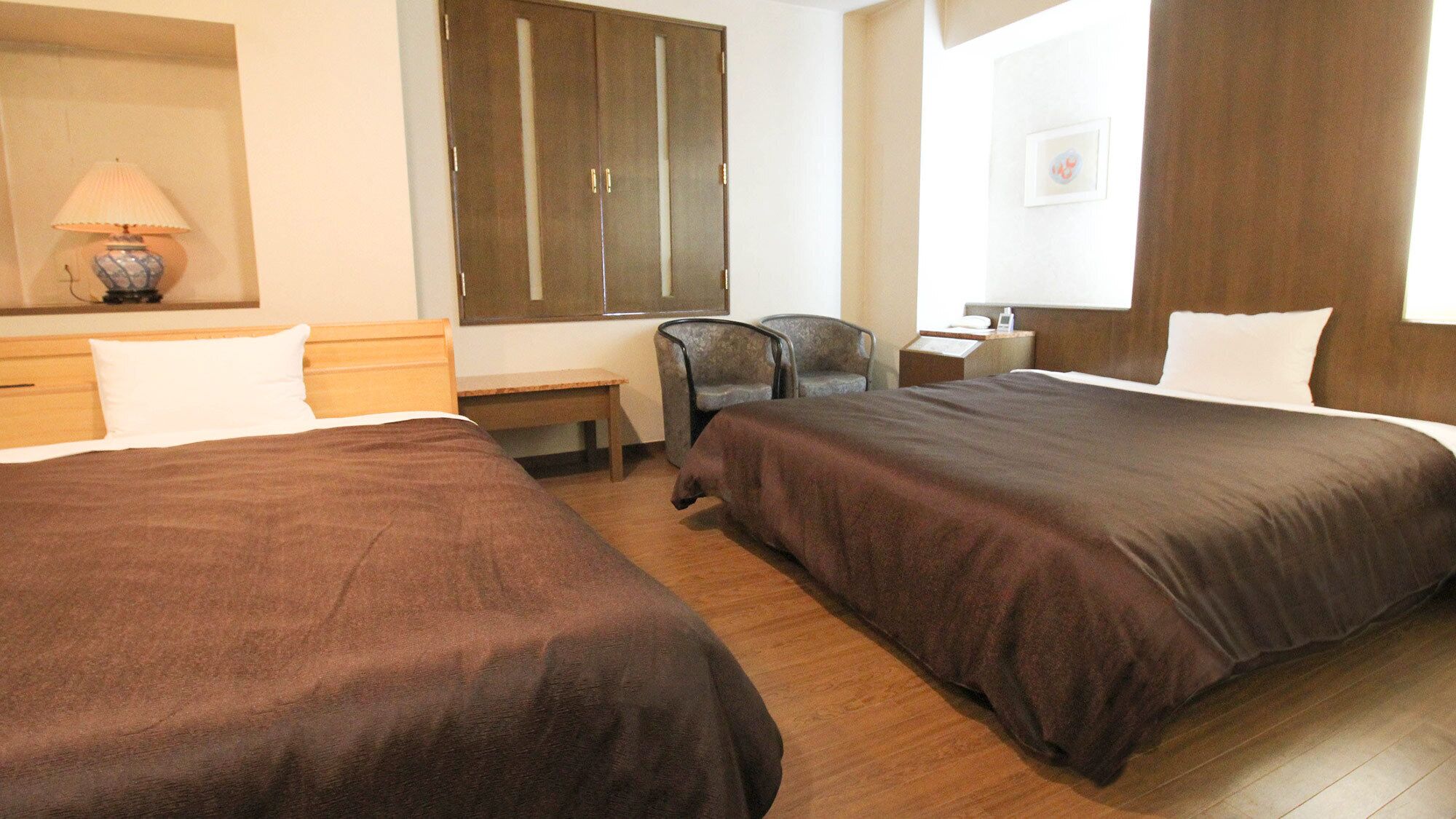 Habitació d'hotel amb dos llits, escriptori, cadira, armari i finestra.