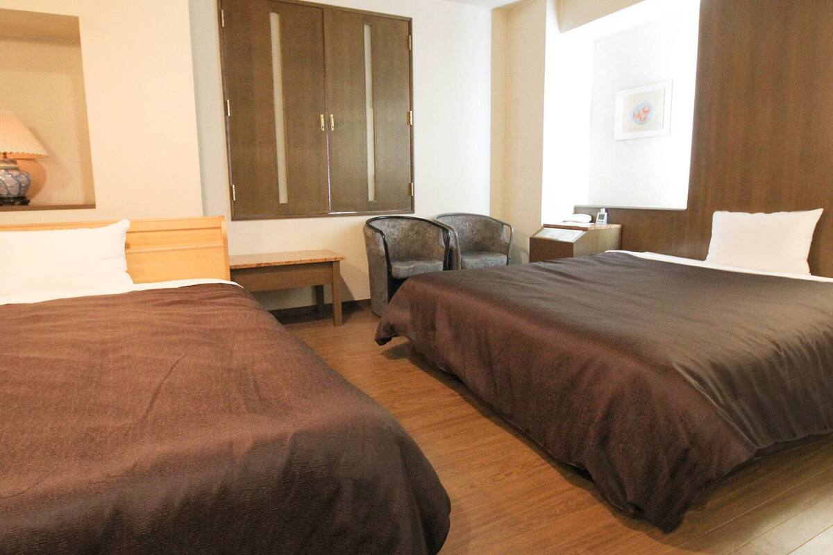 Une chambre d’hôtel avec deux lits, un bureau, une chaise, une armoire et une fenêtre.