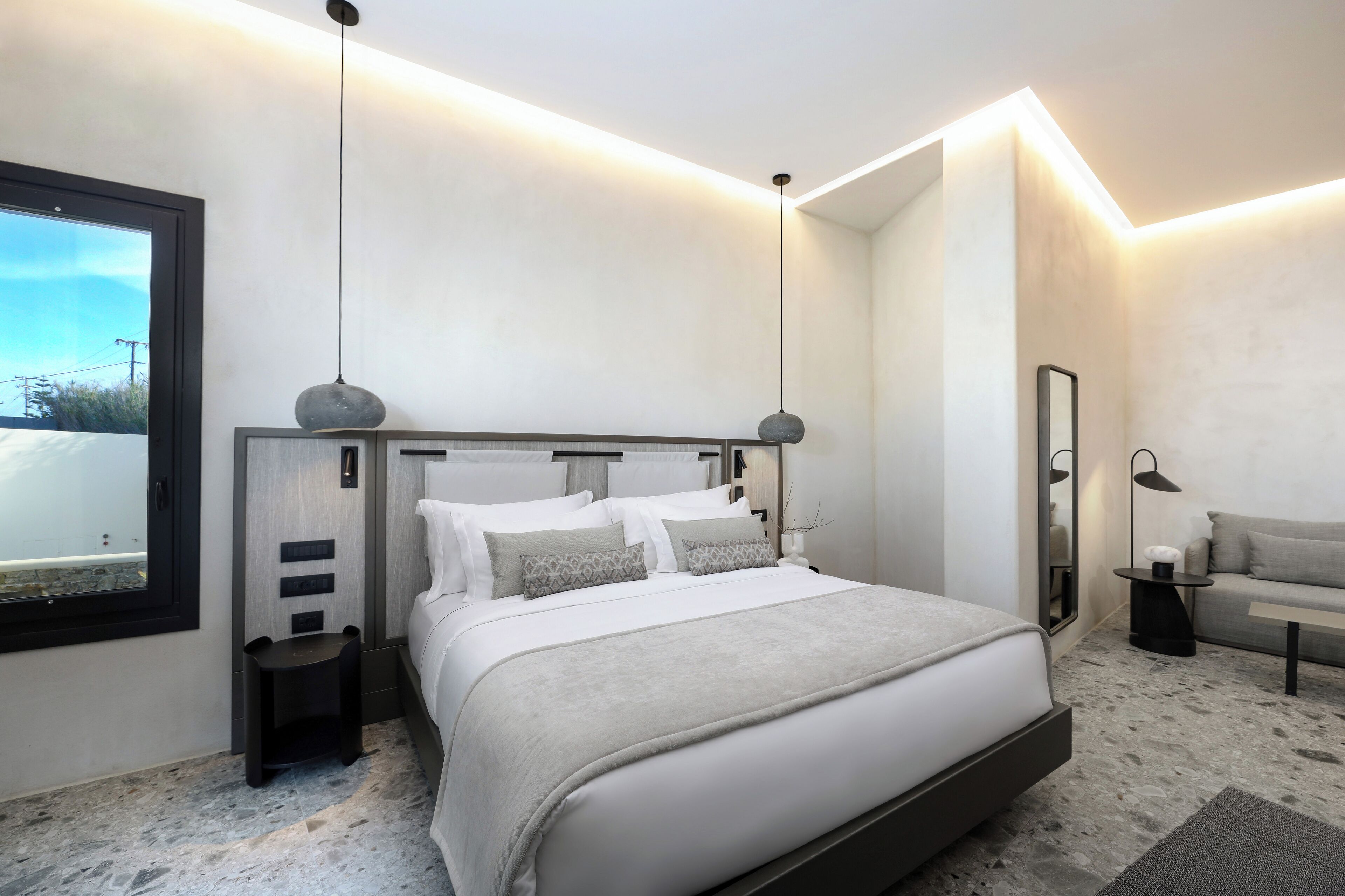 A modern bedroom with a large bed, bedside tables, a nightstand, a sofa, and a mirror.