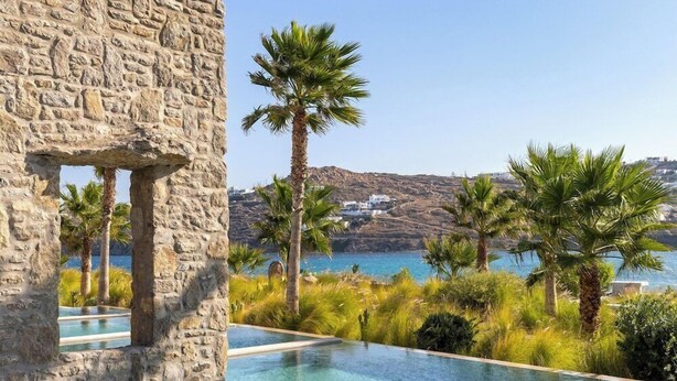 Un edificio de piedra con vistas a un mar azul claro y palmeras.