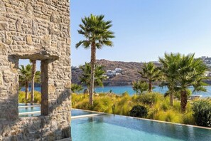 A stone building with a view of a clear blue sea and palm trees. - Aeonic Suites and Spa - Adults Only (Mykonos)
