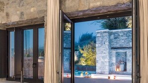 Un interior moderno con una pared de piedra, una bañera negra y vistas a una zona de piscina exterior.