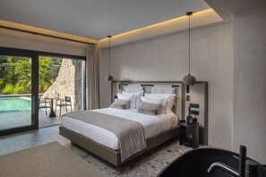 A modern bedroom with a large bed, a built-in desk, and a view of a swimming pool. - Aeonic Suites and Spa - Adults Only (Mykonos)