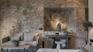 Una habitación acogedora con pared de piedra, un sofá, una mesa baja, una mesita con una planta y una cama.