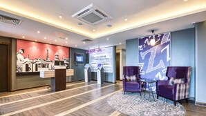 A hotel reception area with a check-in counter, a digital screen, and a seating area with purple chairs. - Premier Inn Newquay (Newquay)