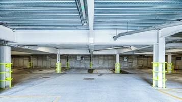 Een overdekte parkeergarage met betonnen vloeren, metalen balken en gele veiligheidsrelingen.