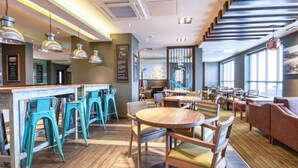 A modern restaurant with a bar area, multiple seating options including round tables and bar stools, and a mix of wooden and upholstered furniture. - Premier Inn Newquay (Newquay)