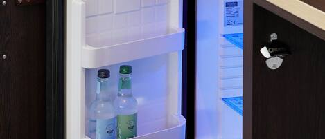 A compact refrigerator with two bottles inside, a coffee maker, and a glass container on top.