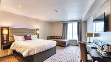 A hotel room with a bed, a desk, a chair, a sofa, a TV, and a window with curtains.