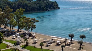Un complexe hôtelier de bord de mer doté de chaises longues, de parasols et offrant une vue sur la mer et les montagnes.