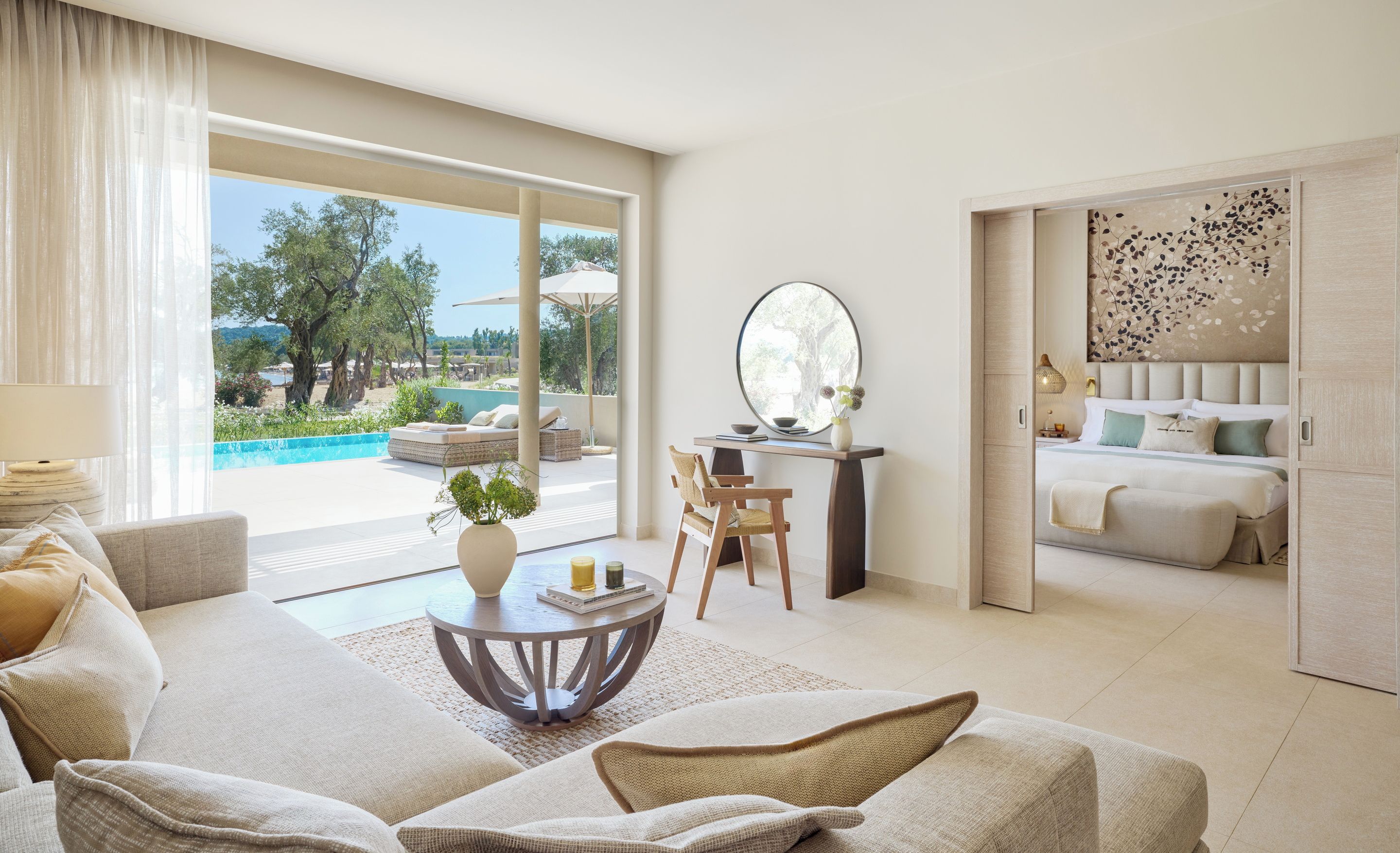 Un vaste espace de vie comprenant un canapé, une table basse ronde et donnant sur une piscine extérieure et un jardin.
