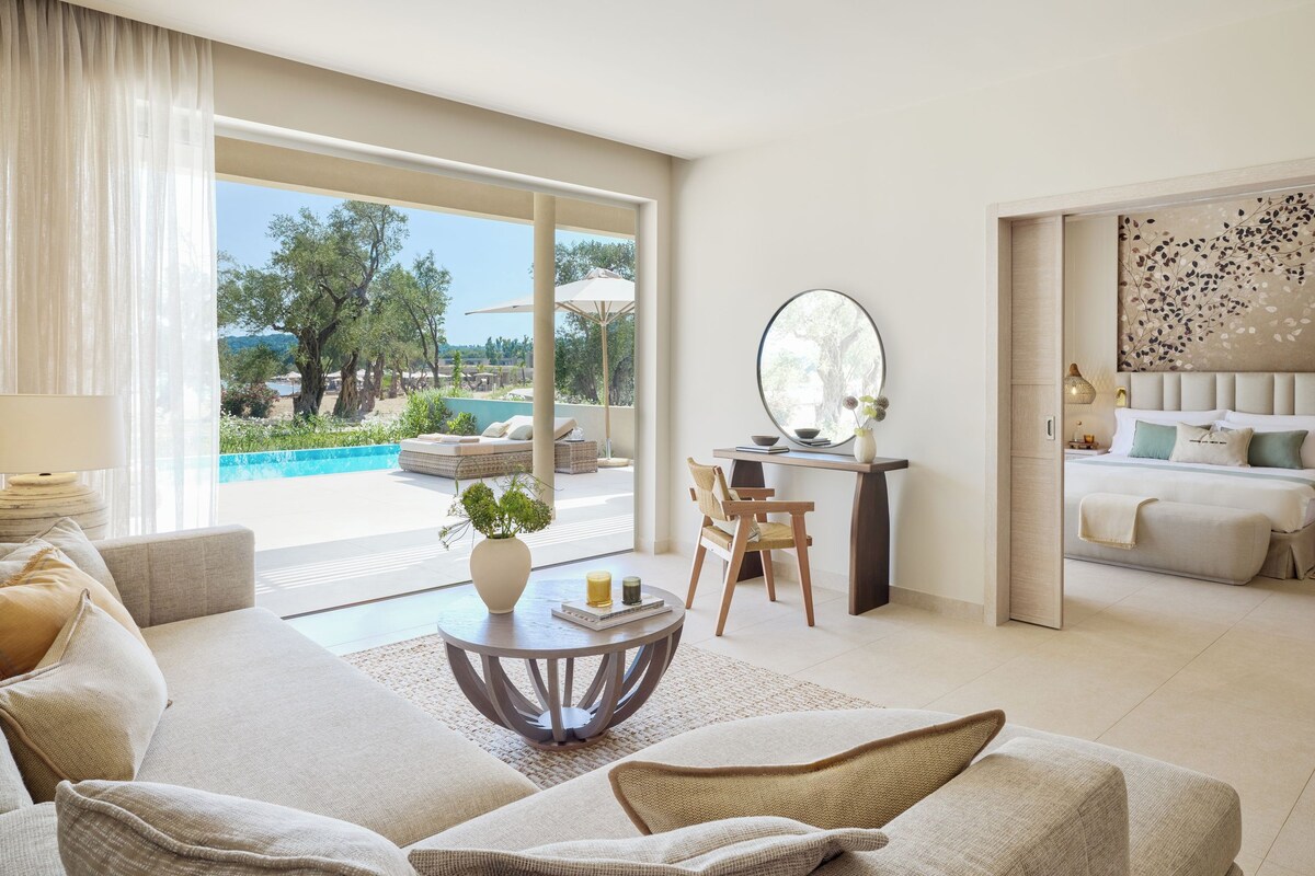 Un amplio salón con sofá, una mesita redonda y vistas a una piscina exterior y jardín.