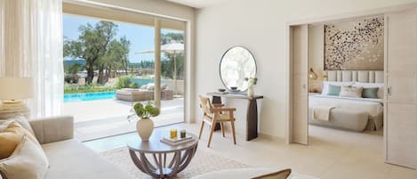 A spacious living area with a sofa, a round coffee table, and a view of an outdoor swimming pool and garden.