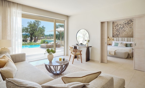 A spacious living area with a sofa, a round coffee table, and a view of an outdoor swimming pool and garden. - Ikos Odisia (Corfu)