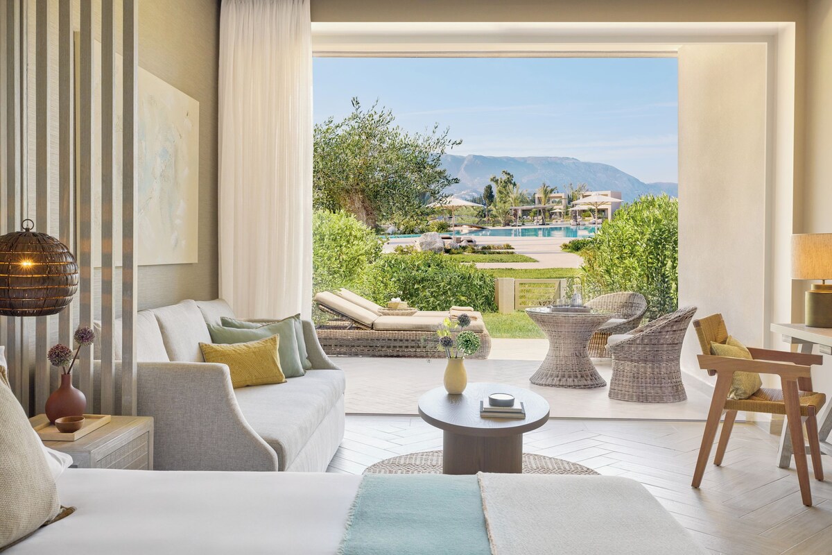 Une chambre d’hôtel dotée d’une grande fenêtre, d’un canapé, d’une table basse et offrant une vue sur une piscine et des montagnes.