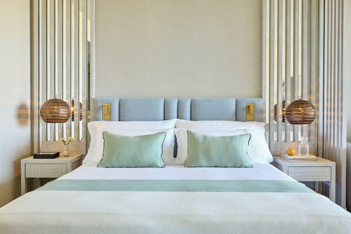 A neatly made bed with pillows, a bedside table with a lamp, and a wall with vertical lines.