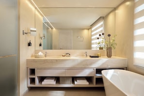 Une salle de bain moderne avec un grand miroir, deux vasques, une baignoire et un vase rempli de fleurs.