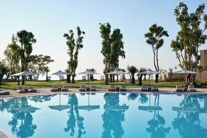 Una piscina con sillas de descanso y sombrillas, rodeada de árboles.