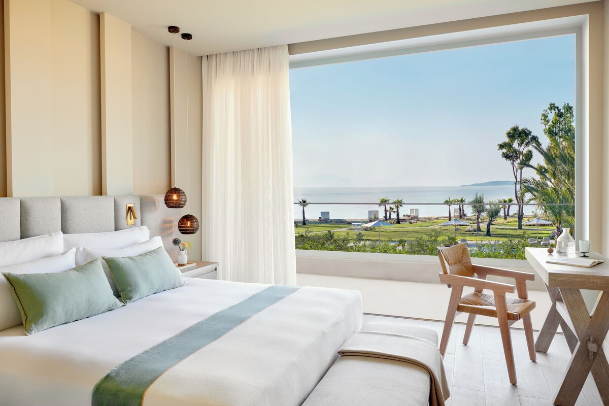 Une chambre d’hôtel avec un grand lit, une vue sur l’océan, un coin repas et un balcon.