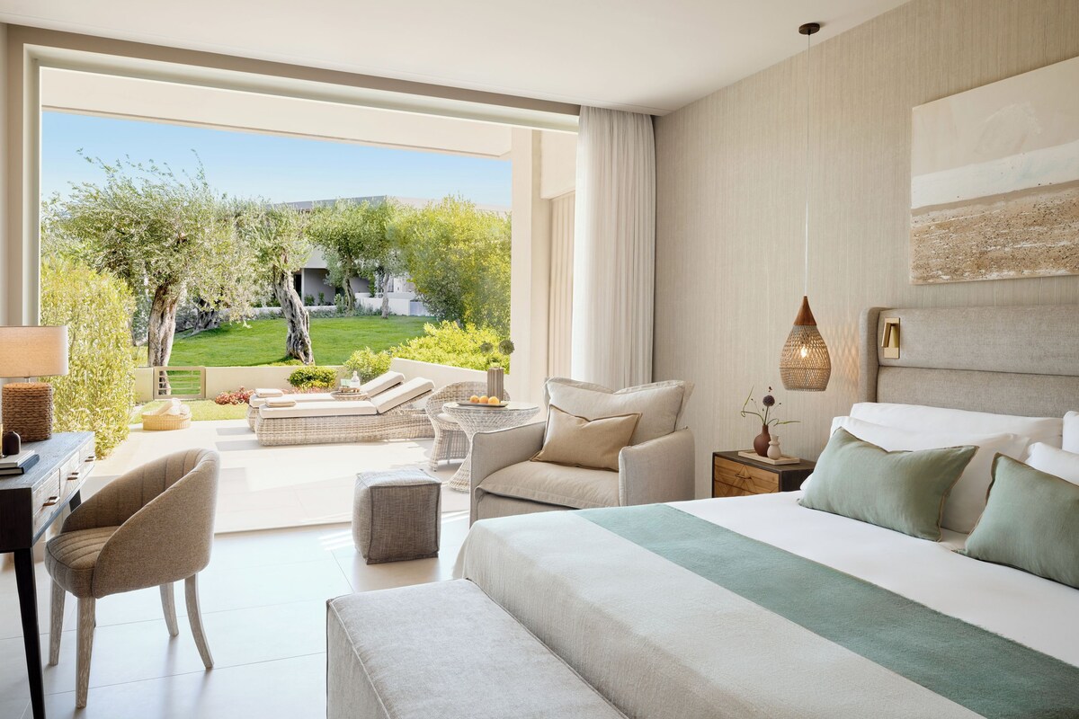 Une chambre d’hôtel moderne dotée d’un grand lit, d’un coin salon avec une table et d’une vue sur un jardin.