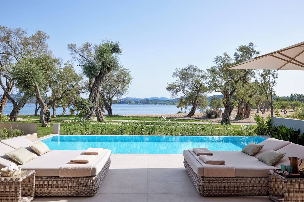 A poolside area with two wicker sofas, a small table, and a view of the sea.