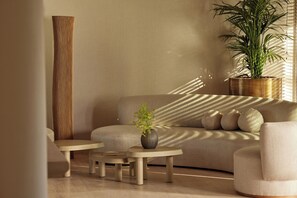 Un salon moderne avec un canapé, deux tables d’appoint, un grand vase contenant une plante et une plante en pot placée contre un mur.
