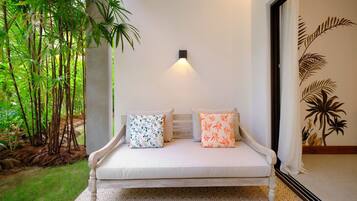 Un banco con dos almohadones, una luz fijada en la pared y un fondo de plantas tropicales.