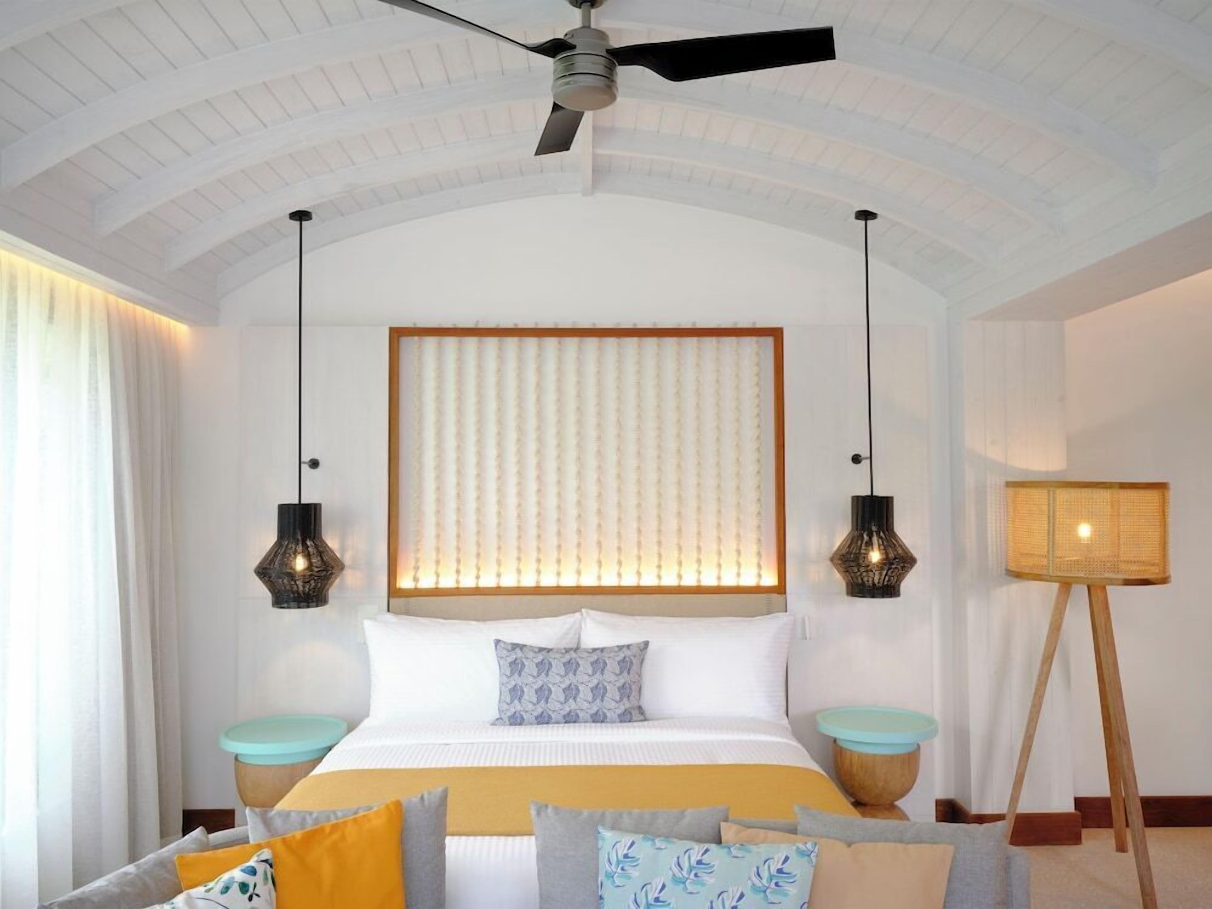 Un dormitorio con una cama grande, dos mesitas de noche, un ventilador de techo y una lámpara de pie.