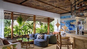 A modern lounge area with a sofa set, a bar area with a drink dispenser, and a view of lush greenery through large windows. - Laila, Seychelles, a Tribute Portfolio Resort (Mahé Island)