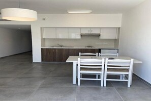 Una cocina moderna con armarios blancos, un lavamanos de acero inoxidable y una zona de comedor con una mesa y sillas blancas.